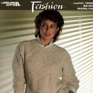 May include: A beige knitted sweater with a textured pattern. The sweater has a round neckline and long sleeves. The model is wearing white pants and a white shirt underneath the sweater.
