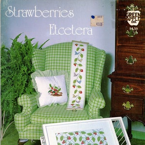 May include: A green and white plaid armchair with a pillow and a framed cross-stitch design of strawberries and leaves. The armchair is in front of a wooden dresser with drawers. The text "Strawberries Etcetera" is at the top of the image. The text "Book 525" is at the bottom left of the image. The text "Designs by Jeanne Bowers and Janet Powers" is at the bottom center of the image. The text "8535" is at the bottom right of the image.