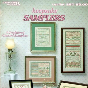 May include: A collection of nine traditional charted sampler cross stitch patterns. The patterns include alphabets, numbers, and various sayings. The patterns are framed and displayed on a pink background.