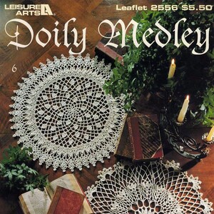 May include: A crochet pattern booklet featuring 9 doilies, with the title "Doily Medley" and the designer's name "Delsie Rhoades". The cover shows two doilies on a wooden surface, with books and candles in the background.