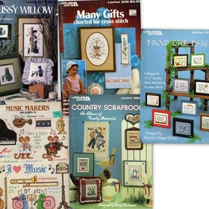May include: A collection of vintage cross-stitch pattern leaflets. Titles include "Pussy Willow," "Many Gifts," "From the Psalms," "Music Makers," and "Country Scrapbook." The leaflets feature framed designs, musical instruments, and family-themed illustrations.