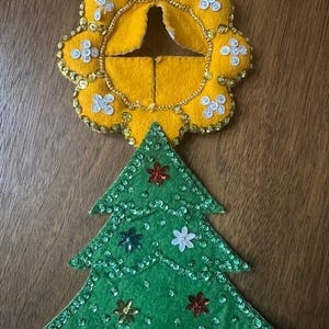 May include: A handmade Christmas tree and star-shaped ornament. The green tree is decorated with sequins and flower-shaped embellishments. The yellow star-shaped ornament is trimmed with gold sequins and a gold chain.