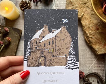 May include: A Christmas card featuring a snowy illustration of a castle with a Scottish flag flying above it. The card reads "Season's Greetings from Lallybroch".