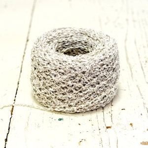 Puede incluir: Un rollo de hilo blanco y gris con una superficie texturizada.