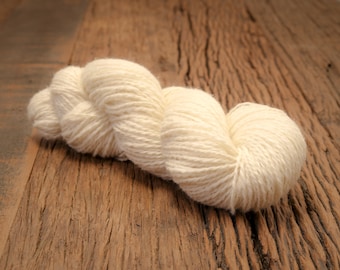 May include: A skein of white yarn, loosely wound and resting on a weathered wooden surface.