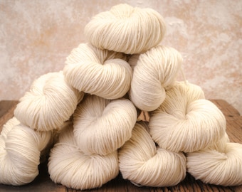 May include: A pile of off-white yarn balls, arranged in a pyramid shape, on a wooden surface.