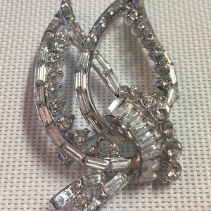 May include: A silver tone brooch with a design of two overlapping leaves, set with clear rhinestones.