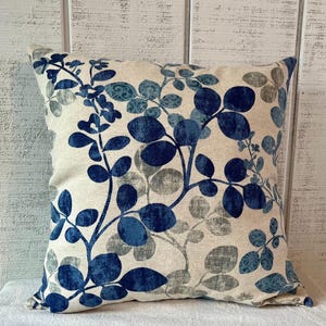 May include: A decorative throw pillow with a blue and gray floral pattern on a cream background. The pillow is made of a soft, textured fabric.