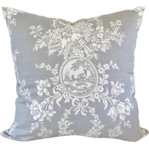 May include: Square decorative pillow with a gray background and a white floral and pastoral design. The central medallion features a bird scene. The pillow has a classic, vintage aesthetic.