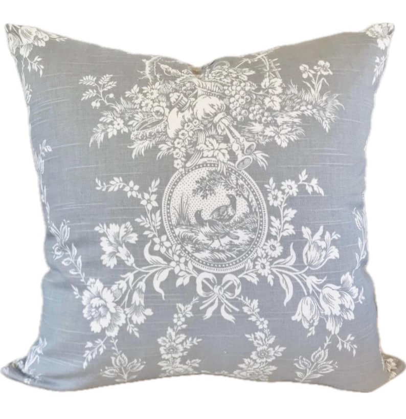 May include: Square decorative pillow with a gray background and a white floral and pastoral design. The central medallion features a bird scene. The pillow has a classic, vintage aesthetic.