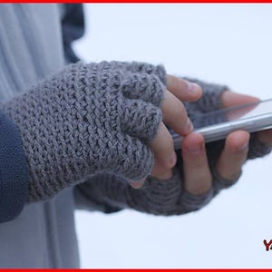 May include: A pair of grey fingerless gloves with a textured knit pattern. The gloves are being worn by a person holding a smartphone.