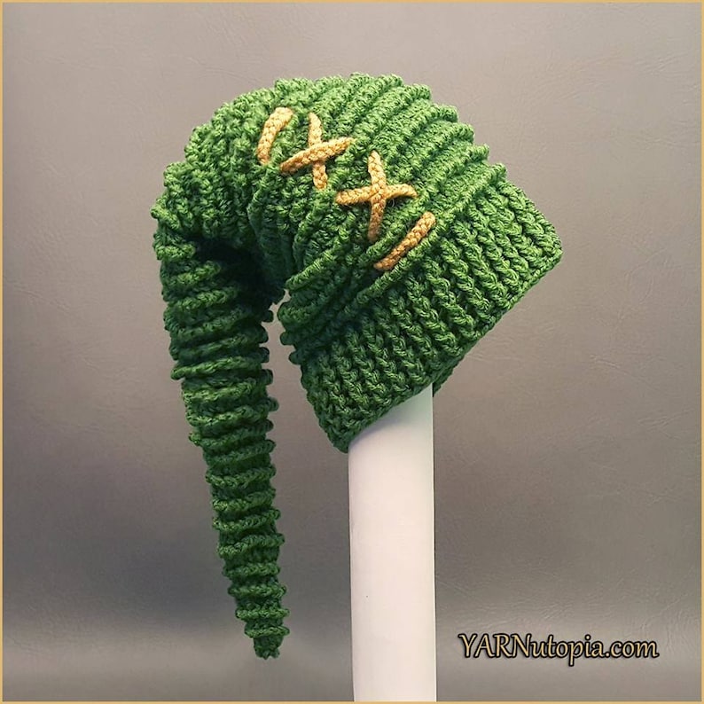 May include: Green crocheted hat with a long, curled tail. The hat has a yellow stitched design on the top.