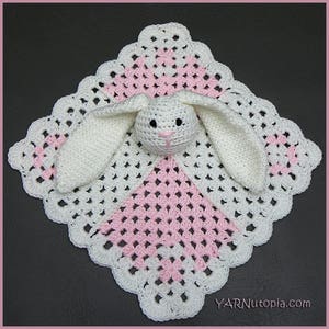 May include: White crocheted baby blanket with a pink and white pattern and a white crocheted bunny attached in the center. The blanket has a scalloped edge.