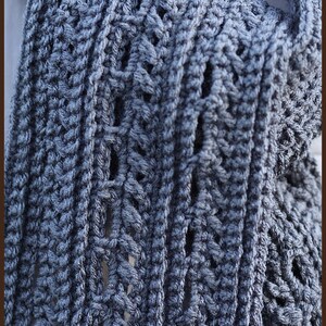 May include: A close-up of a gray crocheted scarf with a textured pattern. The scarf is folded in half and the edges are visible.