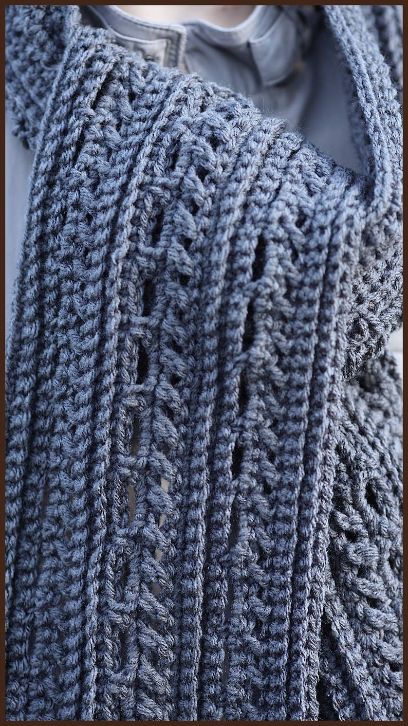 May include: A close-up of a gray crocheted scarf with a textured pattern. The scarf is folded in half and the edges are visible.
