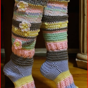 Puede incluir: Un par de calcetines de punto de ganchillo de color a rayas hasta la rodilla con adornos florales. Los calcetines están hechos con una variedad de colores, incluyendo gris, rosa, amarillo y azul.
