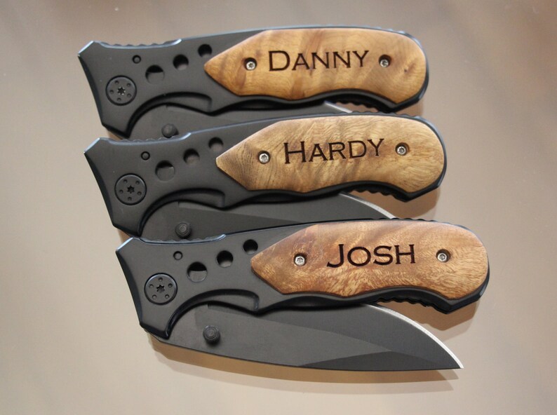 May include: Three personalized pocket knives with wooden handles. The handles are engraved with the names "DANNY", "HARDY", and "JOSH".