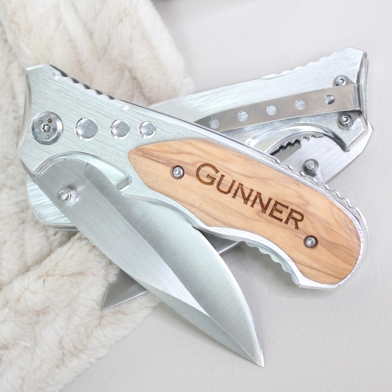 May include: A silver pocket knife with a wooden handle engraved with the name "GUNNER".