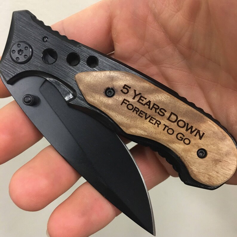 May include: A black pocket knife with a wooden handle engraved with the text "5 Years Down Forever To Go".