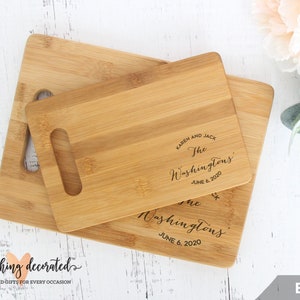 May include: Two wooden cutting boards with a handle. The smaller board is on top of the larger board. Both boards are engraved with the text "Karen and Jack The Washingtons June 6, 2020".