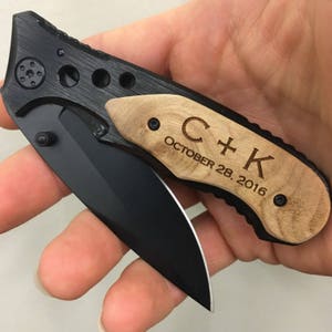 May include: A black folding pocket knife with a wooden handle. The handle is engraved with the initials "C+K" and the date "October 28, 2016".