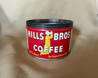 May include: A vintage cylindrical metal Hills Bros Coffee can with a red exterior. The label features white text reading Hills Bros Coffee, Red Can Brand, and The Original Vacuum Pack, along with a graphic of a figure in a yellow robe drinking coffee.