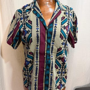 May include: Short-sleeved button-down shirt with a geometric pattern in beige, teal, burgundy, and black. The shirt is displayed on a mannequin. The collar and center placket are burgundy.