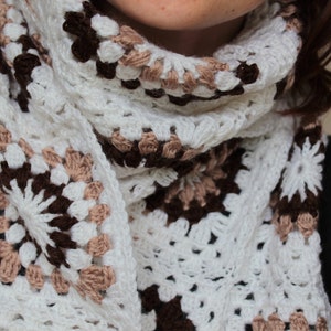 May include: A white crocheted scarf with brown and beige accents. The scarf is made of a delicate, lacy yarn and has a fringed edge.