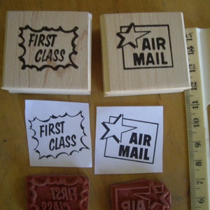 May include: Wooden stamps with the text "FIRST CLASS" and "AIR MAIL" in black ink. The "AIR MAIL" stamp features a star within a square. Includes printed paper versions and a ruler for scale.