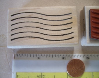 May include: Two wooden rubber stamps. One stamp features six curved black lines. The other has a red rubber surface with parallel curved lines. A ruler and a penny are also in the image.