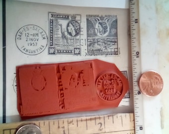 May include: A collection of vintage stamps and a red rubber stamp are shown. The stamps display text and images, including a giraffe and a portrait. The rubber stamp has a circular design with text. A penny and a ruler are also present.
