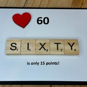 Op de afbeelding: Een rechthoekige wenskaart met een witte achtergrond en een zwarte rand. Het bevat een rood hartpictogram, het getal 60 en houten lettertegels die het woord SIXTY spellen. Onder de tegels staat de tekst: is only 15 points!
