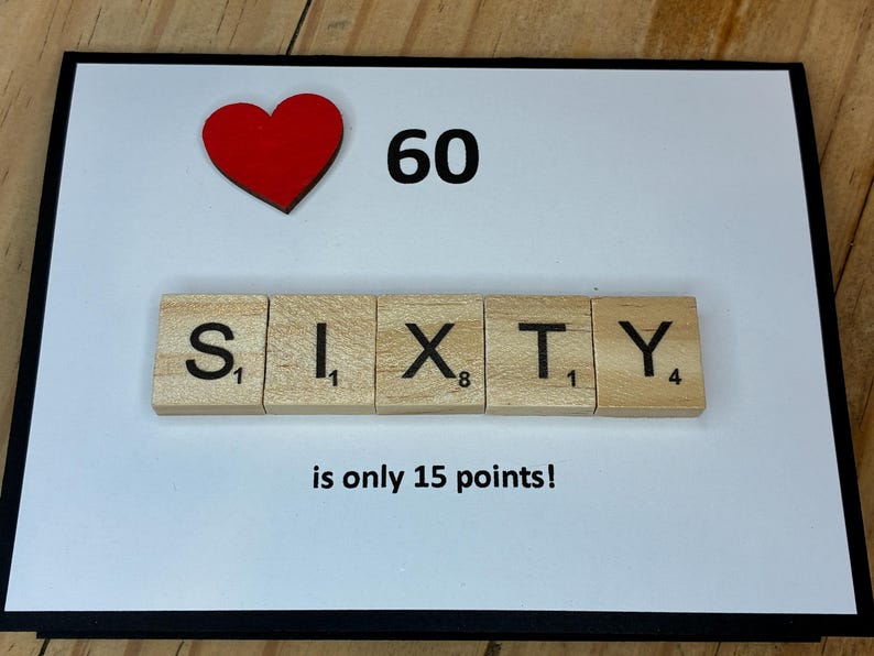 Op de afbeelding: Een rechthoekige wenskaart met een witte achtergrond en een zwarte rand. Het bevat een rood hartpictogram, het getal 60 en houten lettertegels die het woord SIXTY spellen. Onder de tegels staat de tekst: is only 15 points!