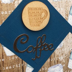 May include: A blue diamond-shaped card with the word "Coffee" in silver script. A wooden circle with a cutout of a coffee cup with polka dots is on the card.