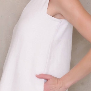May include: A white sleeveless dress with a scoop neck and a side pocket. The dress is made of a textured fabric.