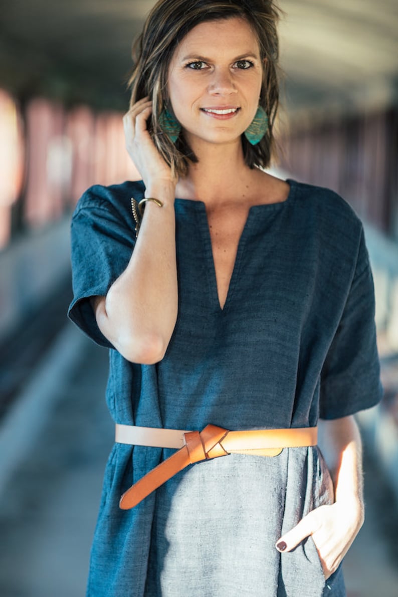 May include: A woman wearing a blue linen dress with a brown leather belt. She is wearing turquoise earrings and a gold bracelet.