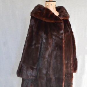 May include: A luxurious, dark brown fur coat with a wide collar and long sleeves. The coat is displayed on a mannequin, showcasing its full length and rich texture. The fur appears soft and plush, perfect for cold weather.