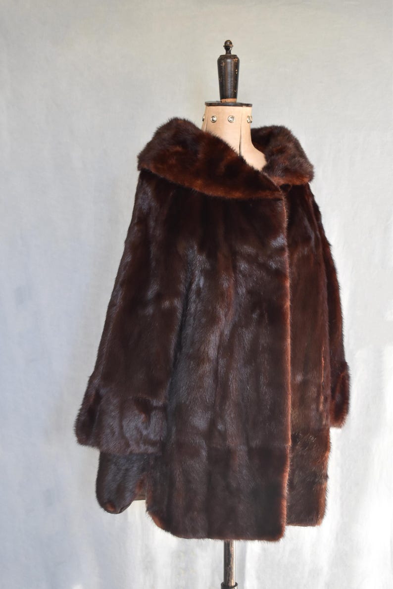 May include: A luxurious, dark brown fur coat with a wide collar and long sleeves. The coat is displayed on a mannequin, showcasing its full length and rich texture. The fur appears soft and plush, perfect for cold weather.