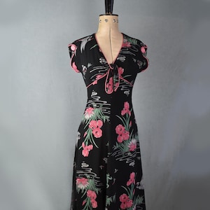 Peut inclure: Une robe vintage noire à imprimé floral avec des fleurs roses, des feuilles vertes et des oiseaux blancs. La robe a un col en V, des manches courtes et un corsage ajusté. La robe est faite d'un tissu léger et a une jupe fluide.