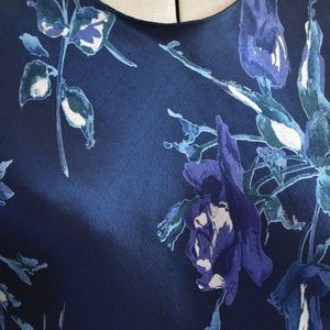 K&ouml;nnte beinhalten: Ein marineblaues Seidenkleid mit einem Blumendruck aus blauen und wei&szlig;en Blumen. Das Kleid hat einen runden Ausschnitt und eine lockere Passform.