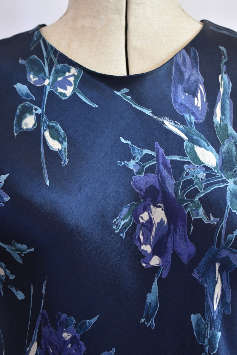 K&ouml;nnte beinhalten: Ein marineblaues Seidenkleid mit einem Blumendruck aus blauen und wei&szlig;en Blumen. Das Kleid hat einen runden Ausschnitt und eine lockere Passform.