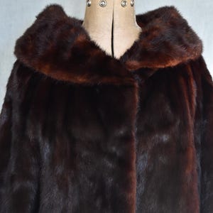 May include: A dark brown fur coat with a wide collar, displayed on a mannequin. The coat has a rich, glossy texture and a deep, luxurious color. The collar is a slightly lighter shade of brown.