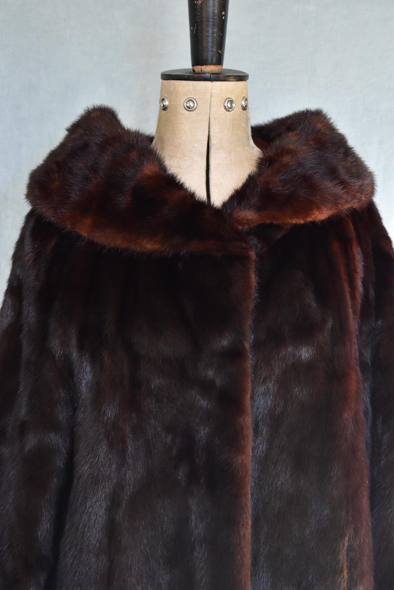 May include: A dark brown fur coat with a wide collar, displayed on a mannequin. The coat has a rich, glossy texture and a deep, luxurious color. The collar is a slightly lighter shade of brown.