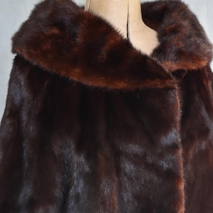 May include: A luxurious dark brown fur coat with a wide collar. The coat is displayed on a mannequin, showcasing its rich texture and deep color. The fur appears soft and plush, suggesting warmth and elegance.