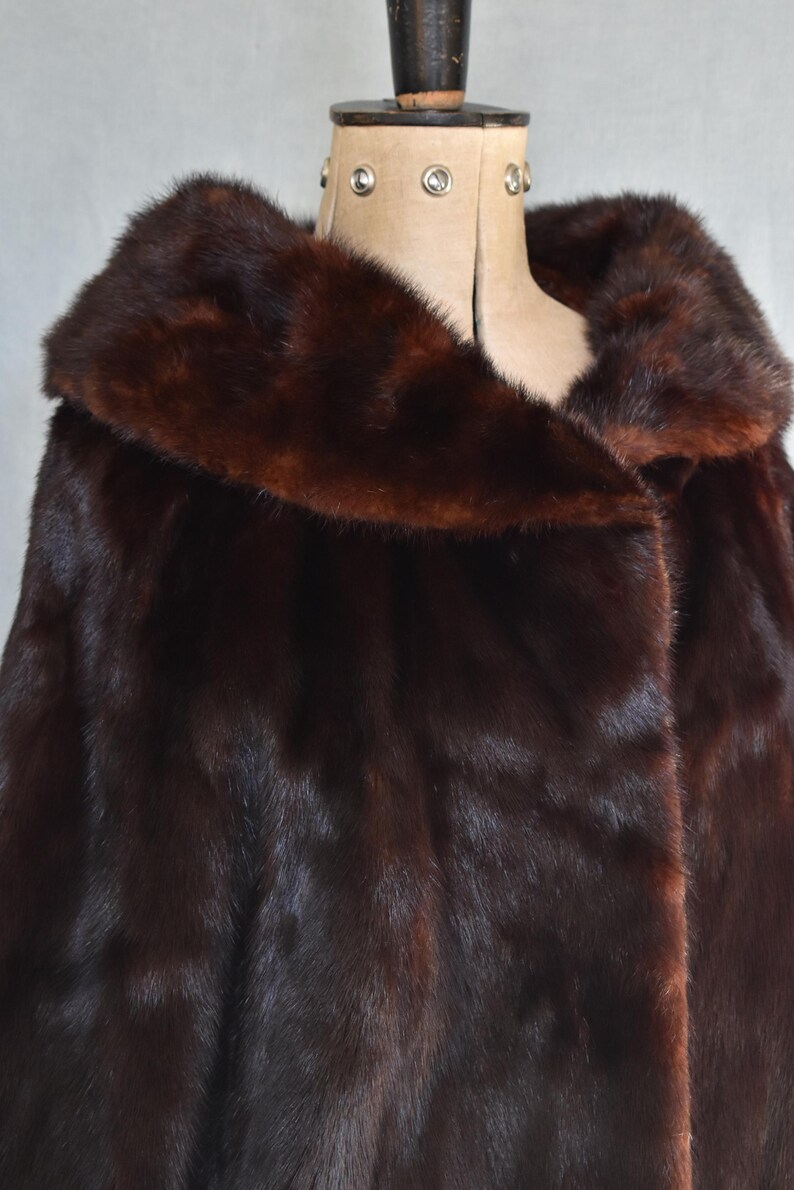 May include: A luxurious dark brown fur coat with a wide collar. The coat is displayed on a mannequin, showcasing its rich texture and deep color. The fur appears soft and plush, suggesting warmth and elegance.