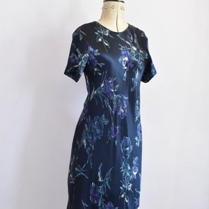 K&ouml;nnte beinhalten: Ein dunkelblaues Satin-Kleid mit einem Blumendruck mit blauen und wei&szlig;en Blumen. Das Kleid hat kurze &Auml;rmel und eine figurbetonte Silhouette.