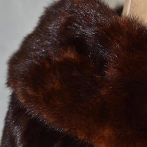 May include: Close-up of a luxurious, dark brown fur coat collar. The fur has a rich, glossy texture with varying shades of brown, creating depth and dimension. The coat appears to be well-maintained and in excellent condition.