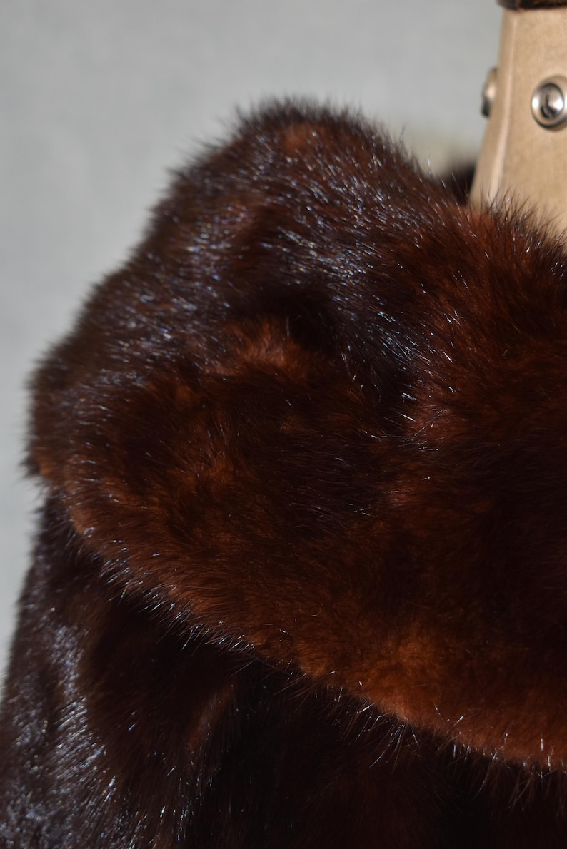 May include: Close-up of a luxurious, dark brown fur coat collar. The fur has a rich, glossy texture with varying shades of brown, creating depth and dimension. The coat appears to be well-maintained and in excellent condition.