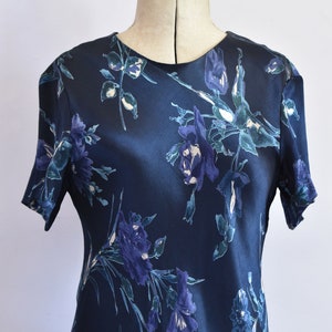 K&ouml;nnte beinhalten: Ein dunkelblaues Satin-Kleid mit einem Blumendruck mit blauen und wei&szlig;en Blumen. Das Kleid hat kurze &Auml;rmel und einen runden Ausschnitt.