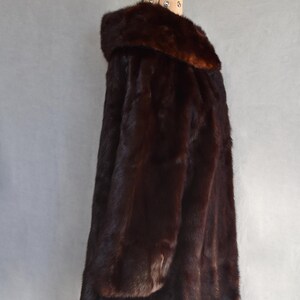 May include: A dark brown fur coat with a wide collar, displayed on a wooden mannequin. The coat has a long, flowing design and appears to be made of soft, luxurious fur. The coat is a rich, deep brown color.